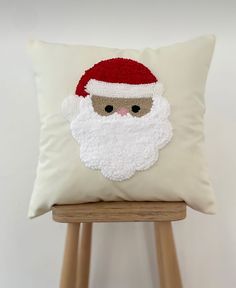 a white pillow with a santa claus face on it, sitting on a wooden stool