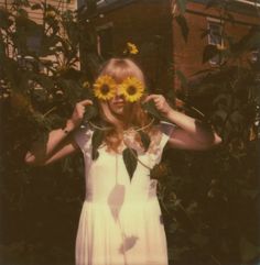 a woman holding up two sunflowers in front of her face