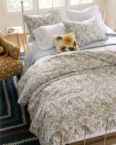 a bed with floral comforter and pillows in a room next to a window,