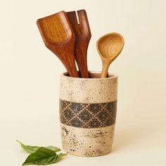 wooden utensils in a ceramic cup on a white surface with a green leaf