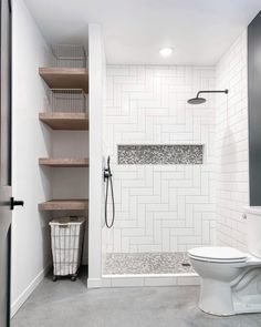 a white toilet sitting in a bathroom next to a walk in shower and wooden shelves