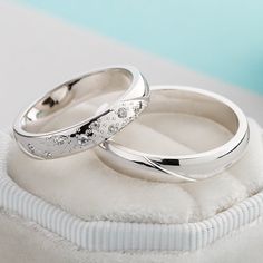 two wedding rings sitting on top of a white cloth covered cushioned pillow in front of a light blue background