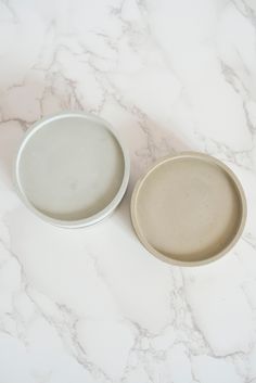 two white plates sitting on top of a marble counter next to each other, one is empty