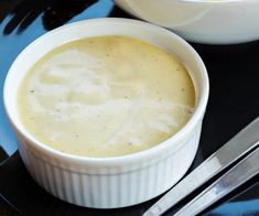 two bowls filled with soup on top of a black plate next to silver utensils