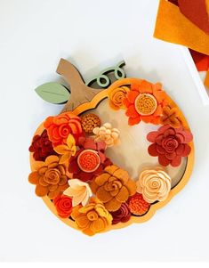 an orange and yellow paper pumpkin with felt flowers on the top, sitting next to other autumn decorations