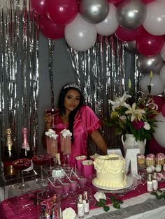 a woman standing in front of a table with a cake on it and balloons hanging from the ceiling