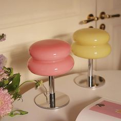 two vases sitting on top of a white table next to pink and yellow flowers