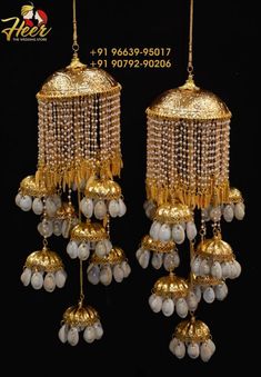 two golden chandeliers with white beads hanging from the sides and gold bells on each side