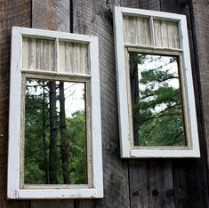 two mirrors are hanging on the side of a building with trees reflected in one window