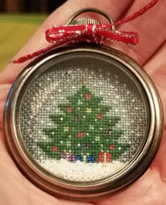 a hand holding a small christmas ornament with a cross stitch tree on it