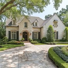 a large brick house surrounded by lush green trees and bushes in front of the entrance