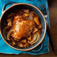 a chicken dish with potatoes and carrots in a blue bowl on a wooden table