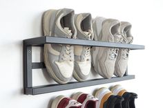 there are many pairs of shoes hanging on the wall and in front of them is a rack with five pairs of sneakers