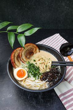 a bowl of ramen with noodles, meats and an egg on the side