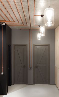 two gray doors in a room with copper piping on the ceiling and lights hanging from the ceiling