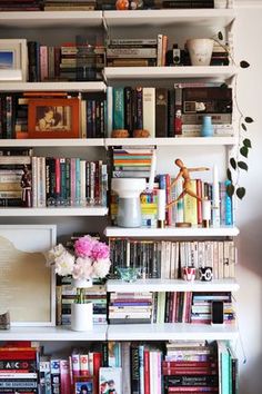 a bookshelf filled with lots of books next to a vase full of flowers