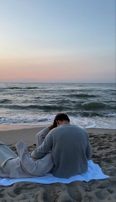 a woman laying on top of a blanket on the beach next to the ocean at sunset