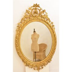 a mannequin's torso in front of a gold framed mirror on a pedestal