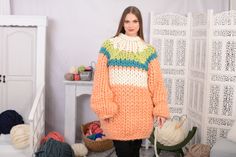 a woman standing in front of a pile of knitted items wearing an orange sweater