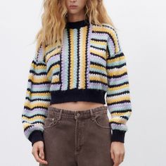 a woman with long blonde hair wearing a multicolored striped sweater and brown pants