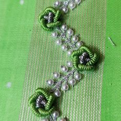 some green flowers and pearls are on a piece of fabric with silver beads hanging from it