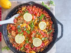 a skillet filled with vegetables and lemons on top of a table