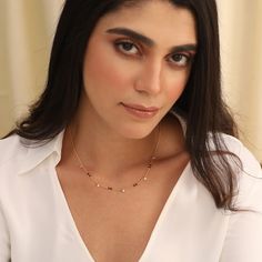 a woman with long hair wearing a white shirt and gold chain necklace on her neck