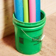 a green bucket filled with lots of different colored paper rolls next to a white wall