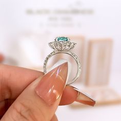 a woman's hand holding an engagement ring with a green stone on the top