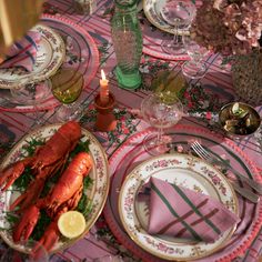 lobsters are on plates with pink napkins and green glassware, along with other dishes