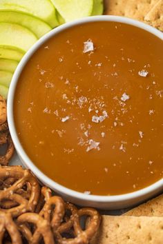 a bowl of caramel sauce surrounded by pretzels, apples and crackers