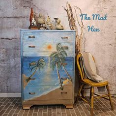 an old dresser with palm trees painted on it and a chair in front of it