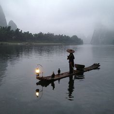 a person on a small boat in the water with two lanterns and some birds perched on it