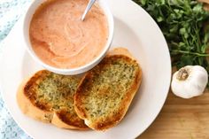 two pieces of bread on a white plate with a bowl of soup in the middle