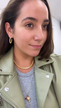 a woman wearing a green leather jacket and gold hoop earrings is looking at the camera