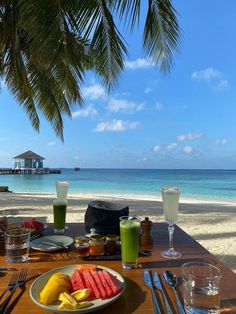 there is a plate of fruit and juice on the table next to the water with a view of the beach