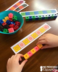 a child's hands playing with legos on a table next to a bowl of colored blocks