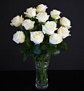 a glass vase filled with white roses on top of a black tableclothed surface