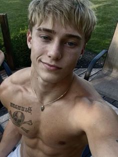 a shirtless young man sitting in a chair with tattoos on his chest and arm