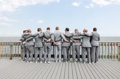 a group of men standing next to each other on top of a wooden deck near the ocean