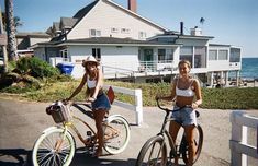 two women riding bikes next to each other in front of a house near the ocean