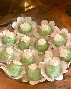 some green and white cupcakes are in a bowl on a wooden table with flowers