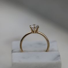 a gold ring with a single diamond on it sitting on top of a marble block