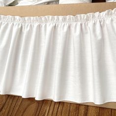 a white bed skirt sitting on top of a wooden floor next to a brown box