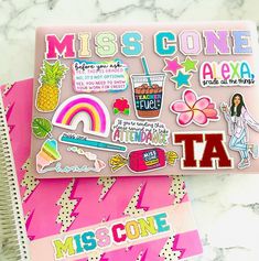 two notebooks with stickers on them sitting next to each other, one is pink and the other is blue