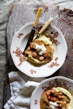 two white plates topped with food on top of a wooden table next to utensils