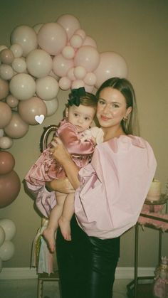 a woman holding a baby in her arms and balloons around her head behind her back