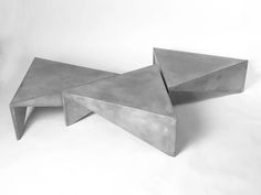 two concrete tables sitting side by side on a white surface, one is shaped like an arrow