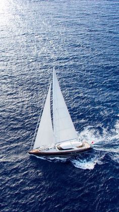 a sailboat sailing in the ocean on a sunny day with blue water behind it