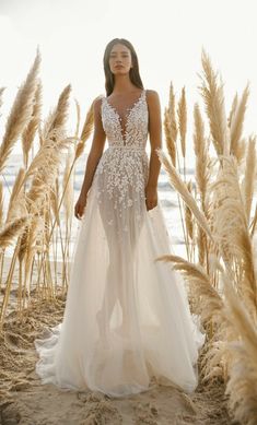 a woman standing on top of a sandy beach next to tall grass and sea oats